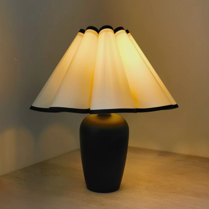 Table lamp with a scalloped cream shade illuminated to create a warm and inviting atmosphere in any home setting.