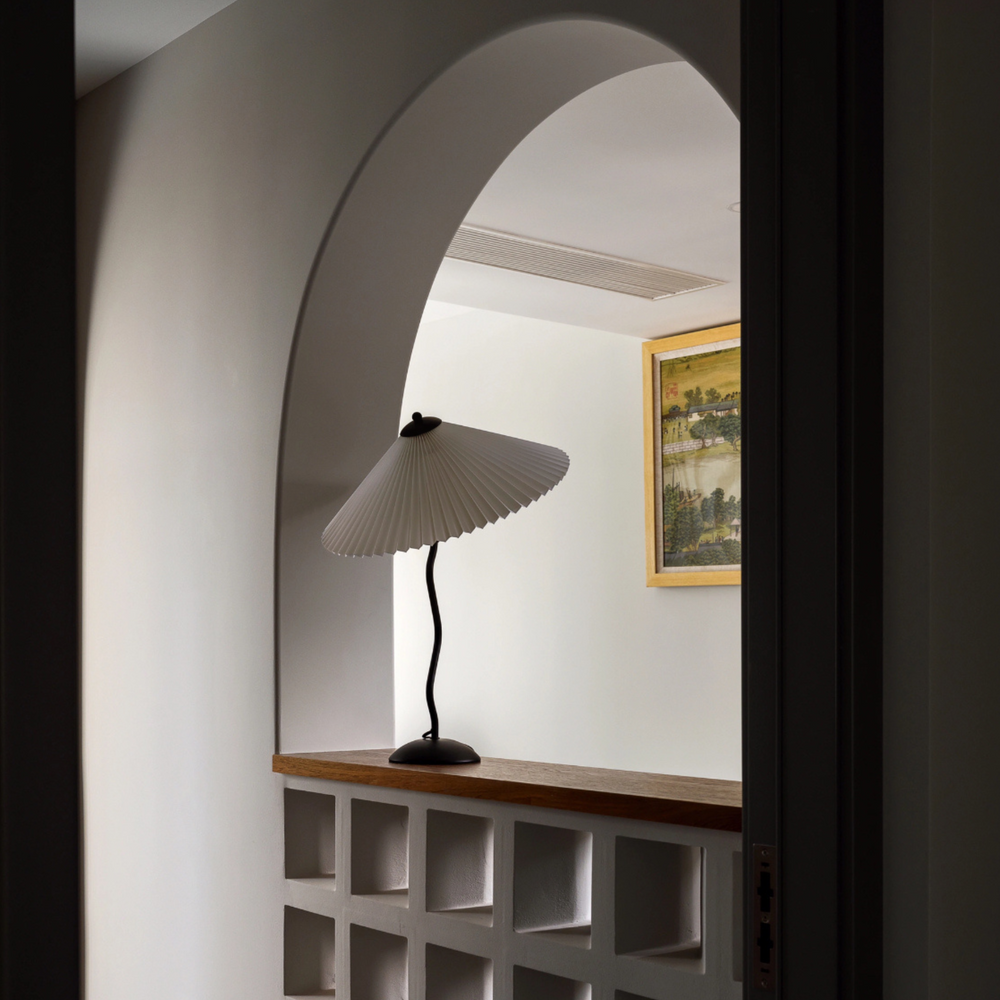 Table lamp with pleated shade, standing gracefully in a modern corner space with clean and artistic elements.