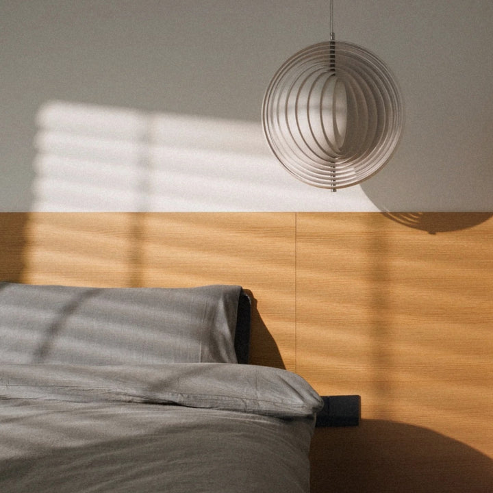 pendant light beside a bed casting shadows across a warm wall.