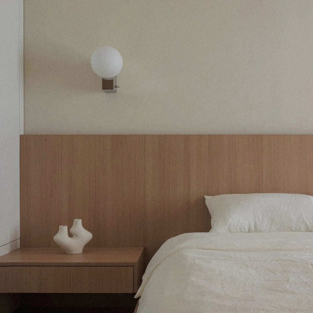 glass globe wall sconce positioned above a bedside surface in a minimal bedroom.