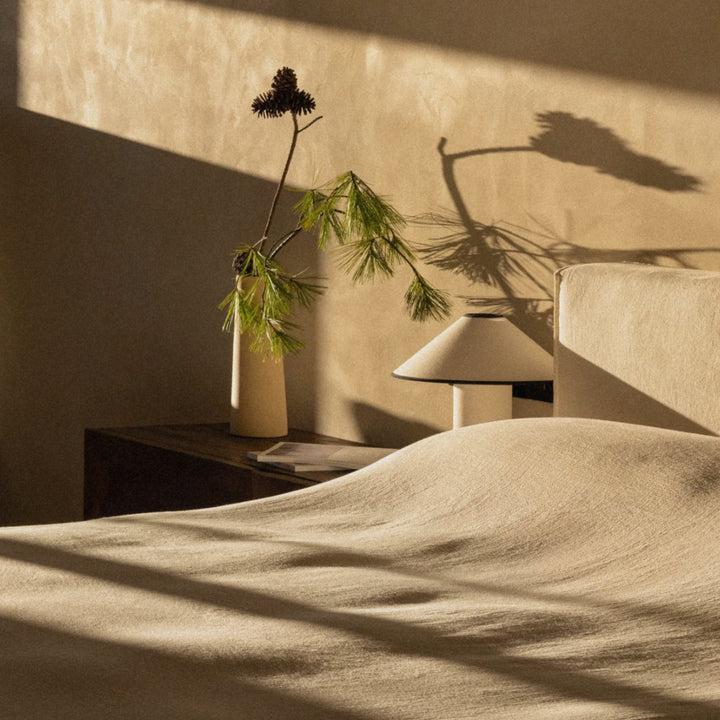 bedside lamp next to a bed with sunlight casting shadows across the wall.