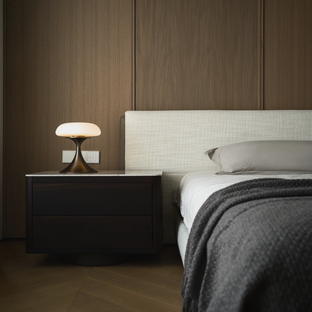 Minimalist lamp with a warm light, placed on a dark wooden bedside table in a contemporary bedroom.