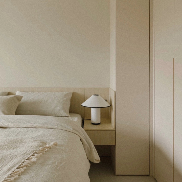 bedside table lamp placed next to a bed in a modern neutral bedroom.