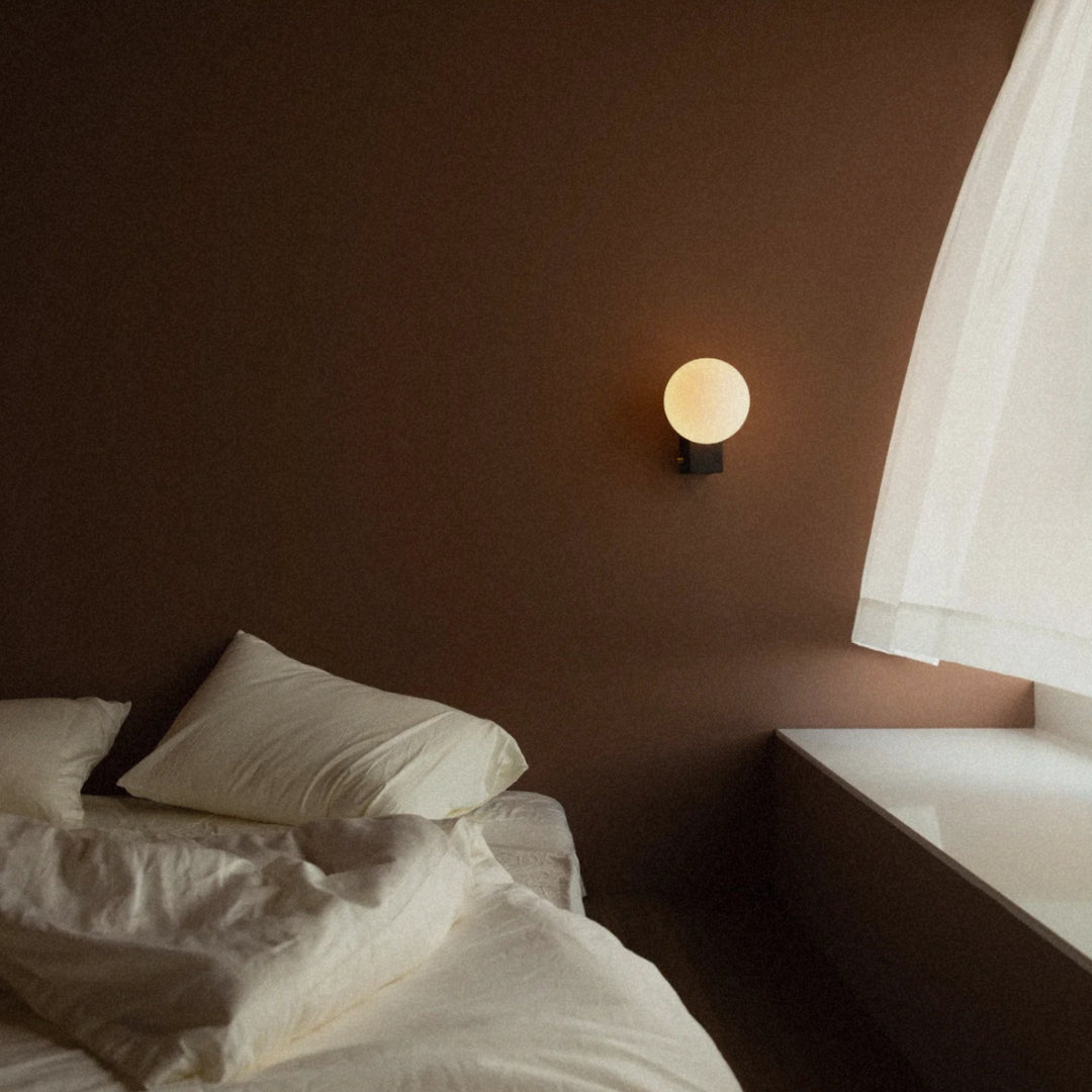 glass globe wall sconce used as bedside wall lighting in a warm bedroom.