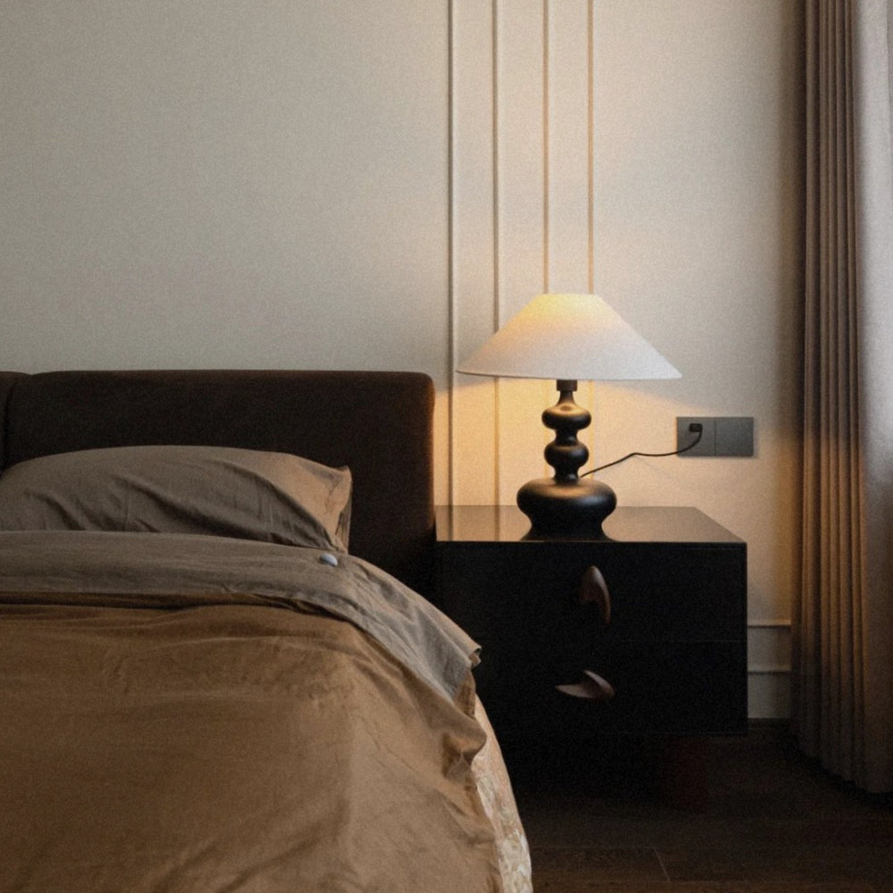 bedside wood table lamp positioned next to a bed with low warm lighting.
