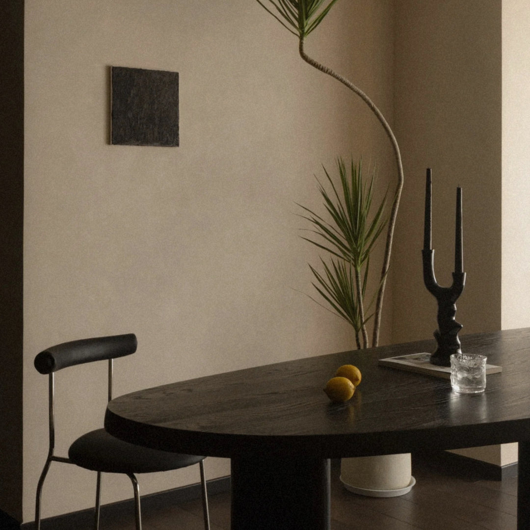 black ceramic candlestick standing on a dark dining table in a warm minimalist interior.