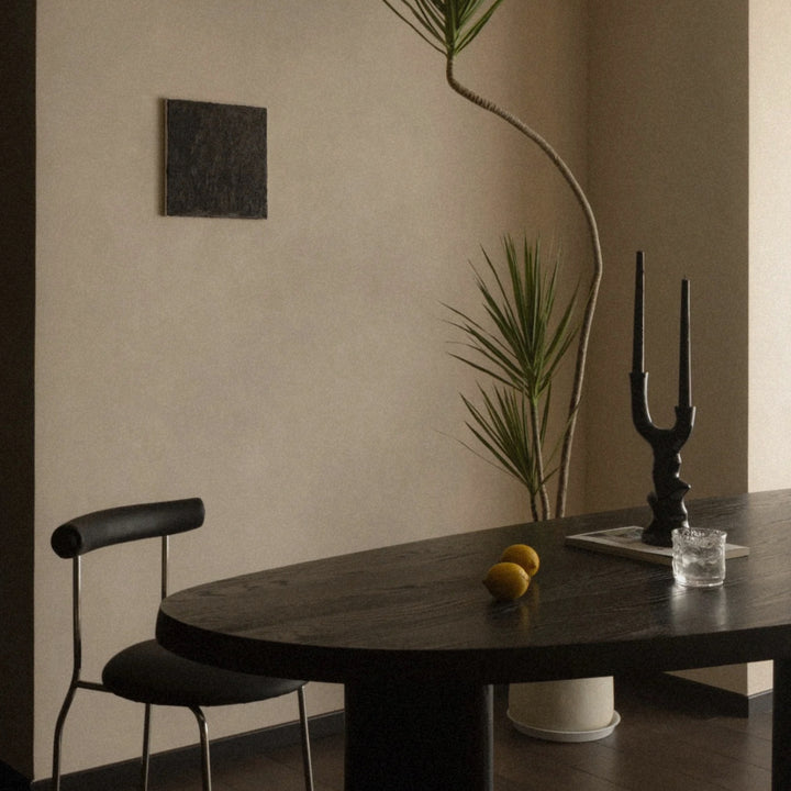 black ceramic candlestick standing on a dark dining table in a warm minimalist interior.