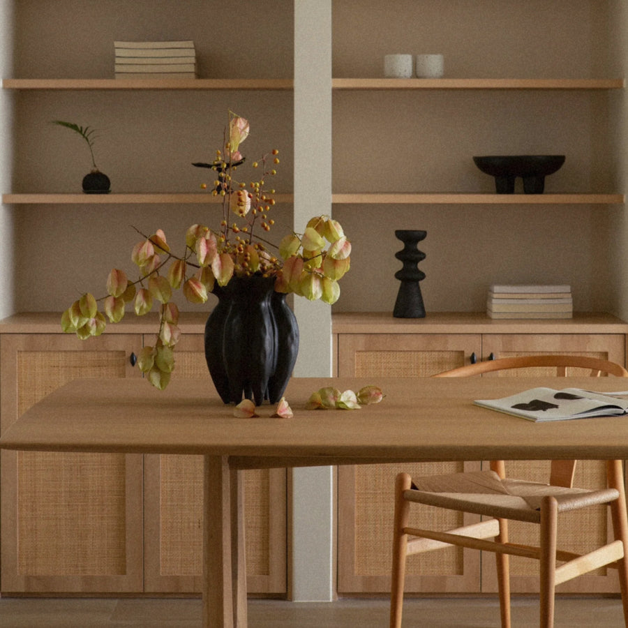 black ceramic vase with branches placed at the center of a wooden dining table.