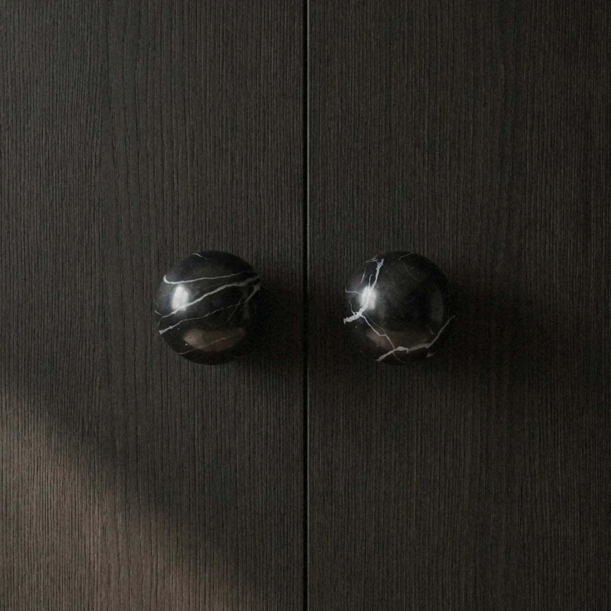 Black marble cabinet knob on dark wood cabinet doors with dramatic shadow detail.