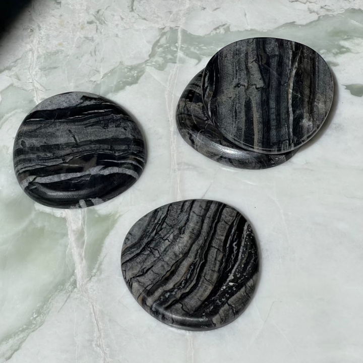 Set of black marble coasters with unique white veining on a white marble table, ideal for modern decor.