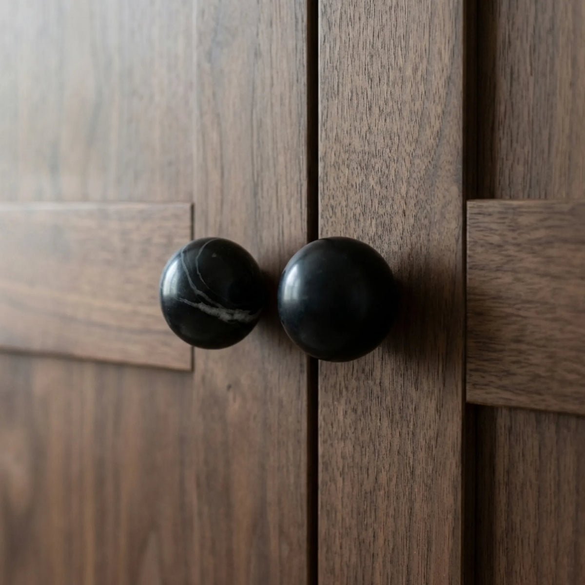 Black marble stone cabinet knobs on dark wood wardrobe doors, for modern bedroom storage.