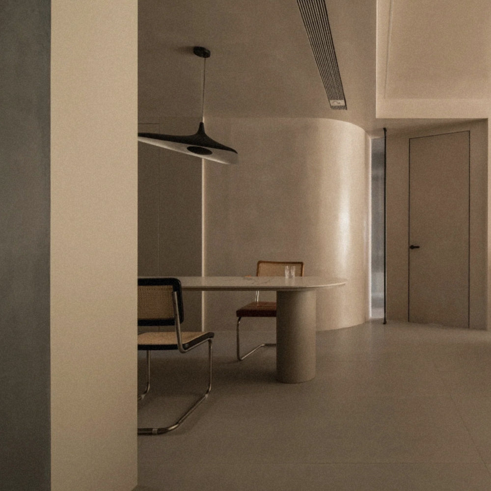black minimalist pendant light suspended above a round dining table in a soft contemporary dining space.