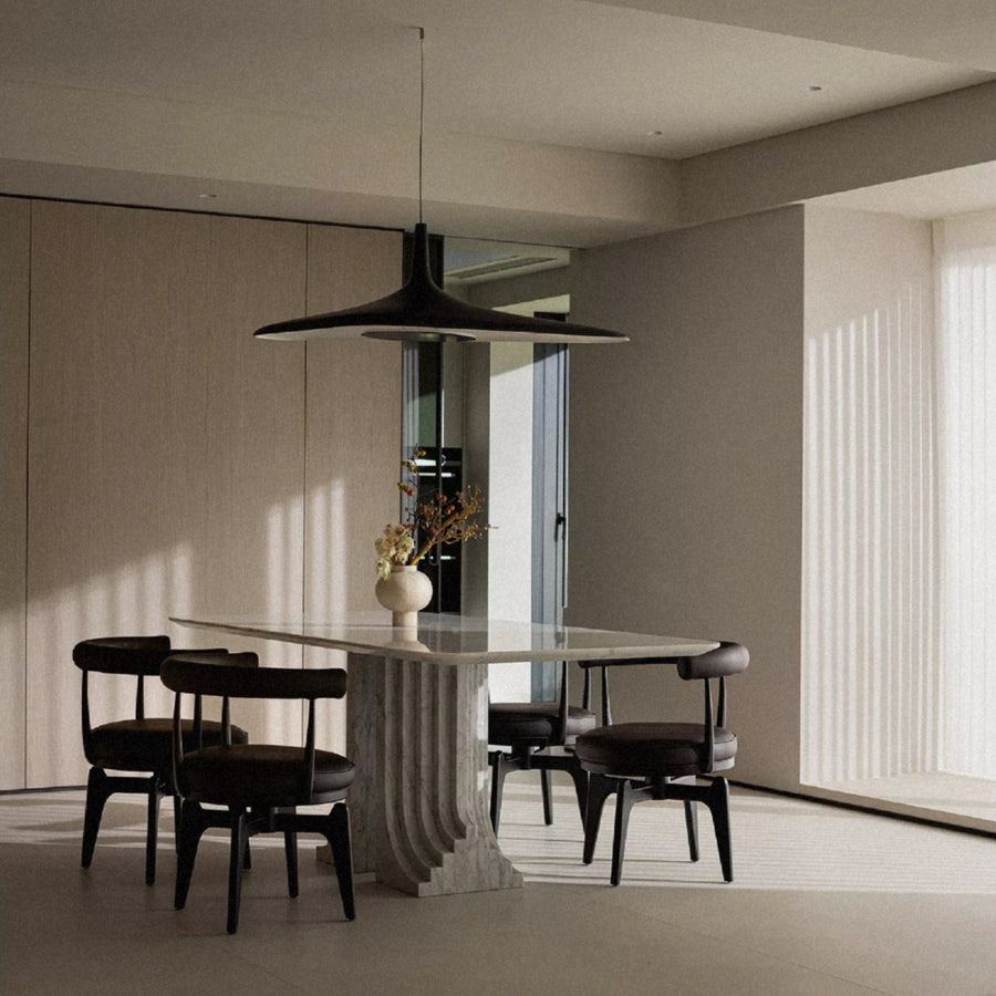 black modern pendant light hanging above a round dining table in a calm minimalist dining room with neutral tones.