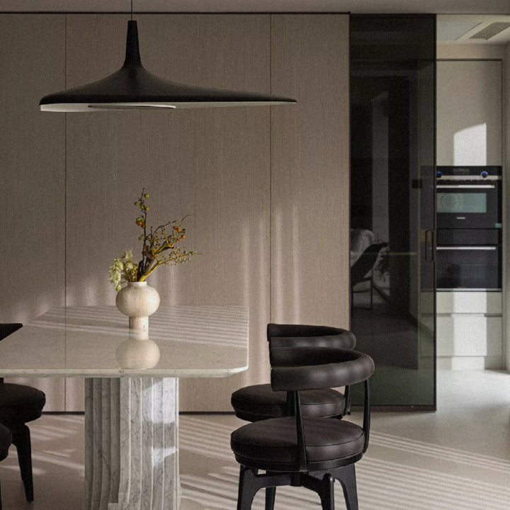 black modern pendant light positioned above a round dining table in a neutral contemporary interior.