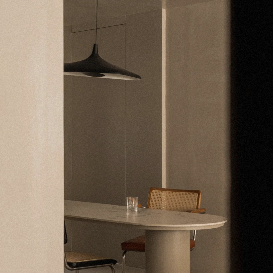black modern pendant light illuminating a small dining area with a round table in a minimalist interior.