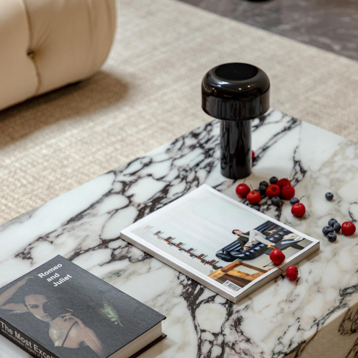 A modern black cordless lamp styled on a statement marble coffee table in a neutral living room with plush seating.