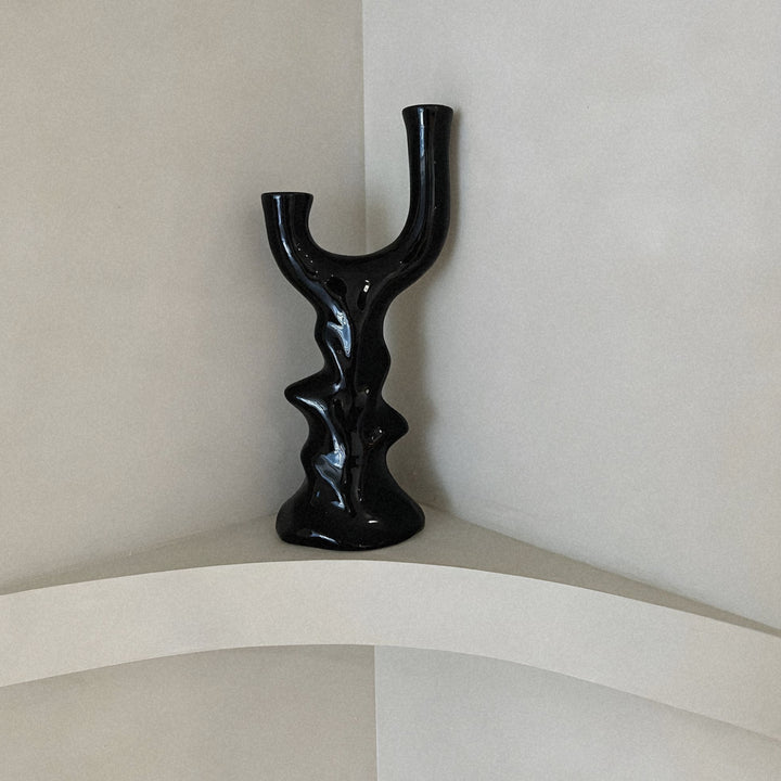 black sculptural ceramic candlestick displayed on a curved wall shelf.