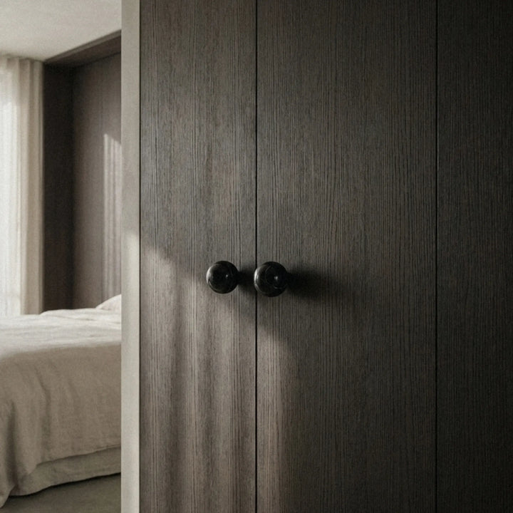 Black stone cabinet knob on dark door in bright entryway, minimalist decorative hardware.
