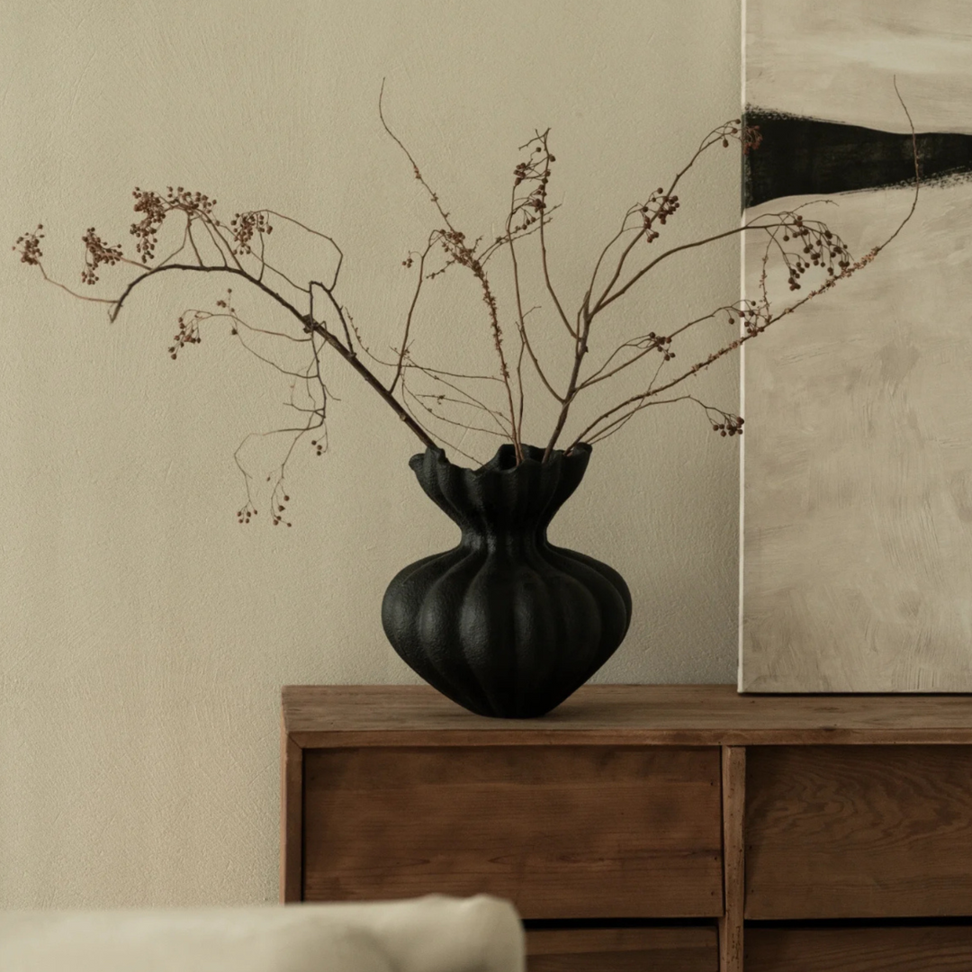 Modern black vase against a neutral backdrop with rustic elements, blending elegance with earthy tones