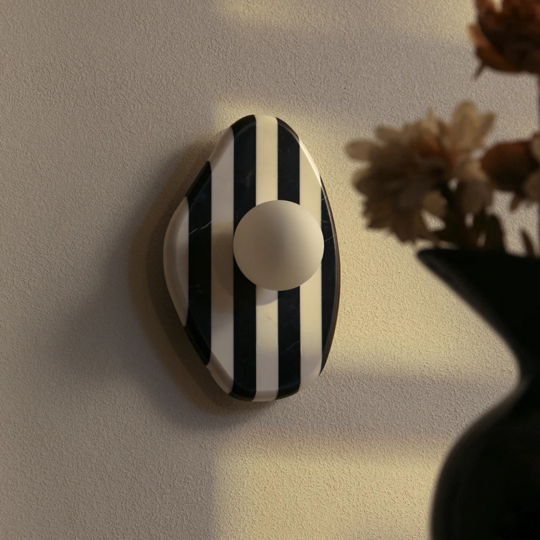 Angled view of black and white striped marble wall lamp with a spherical light, modern artistic design.