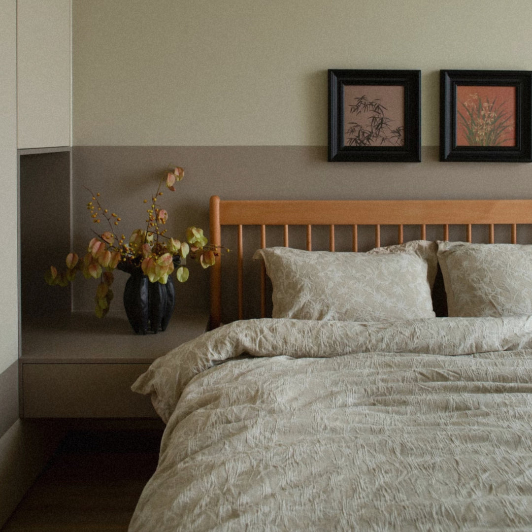 ceramic vase holding branches placed on a wooden console beside the bed.