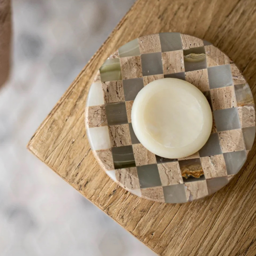 Checkerboard tray from jade marble and travertine, used as a base for a candle on a wooden surface.