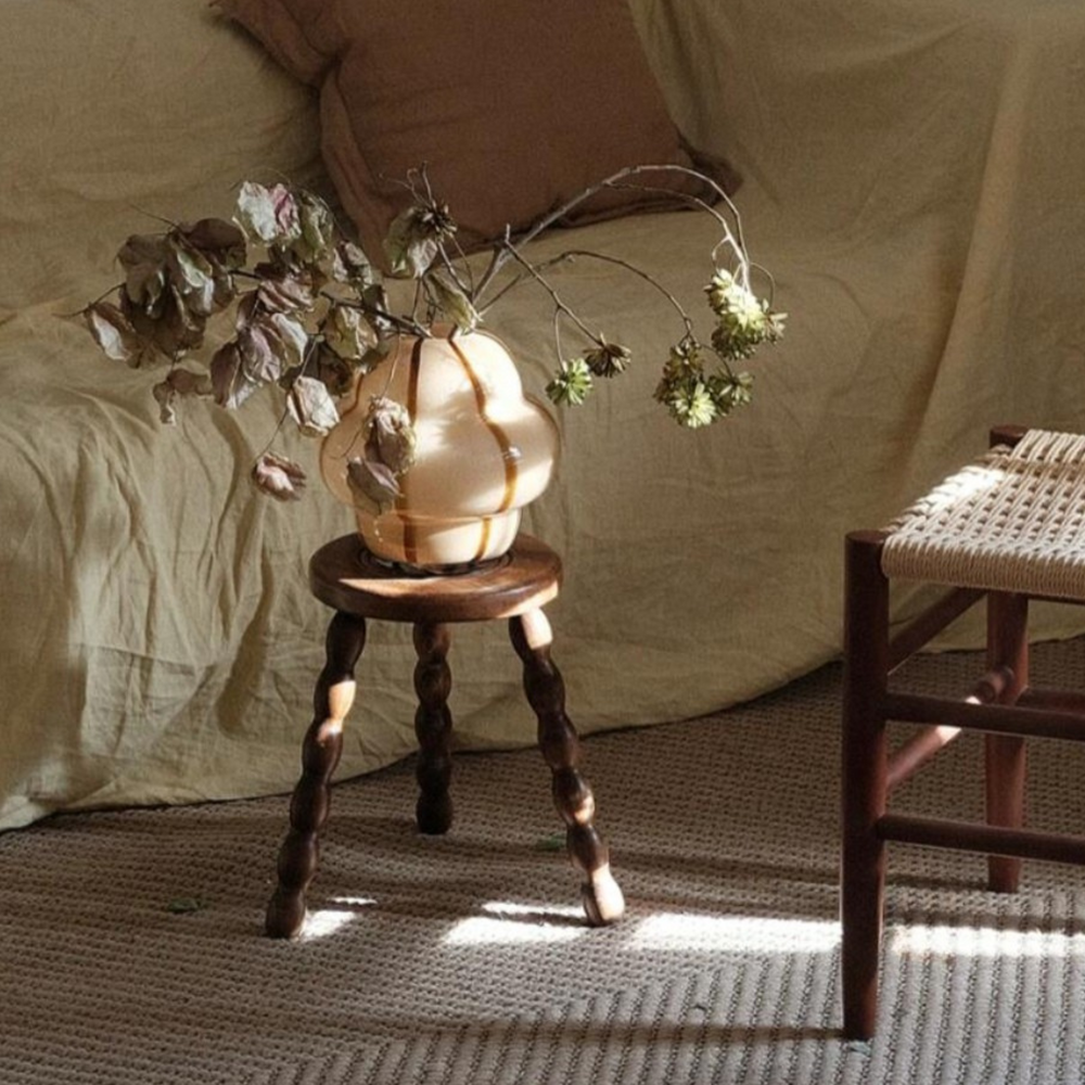 Chubby glass vase with brown accents, displayed on a wooden stool in a minimalist rustic setting.