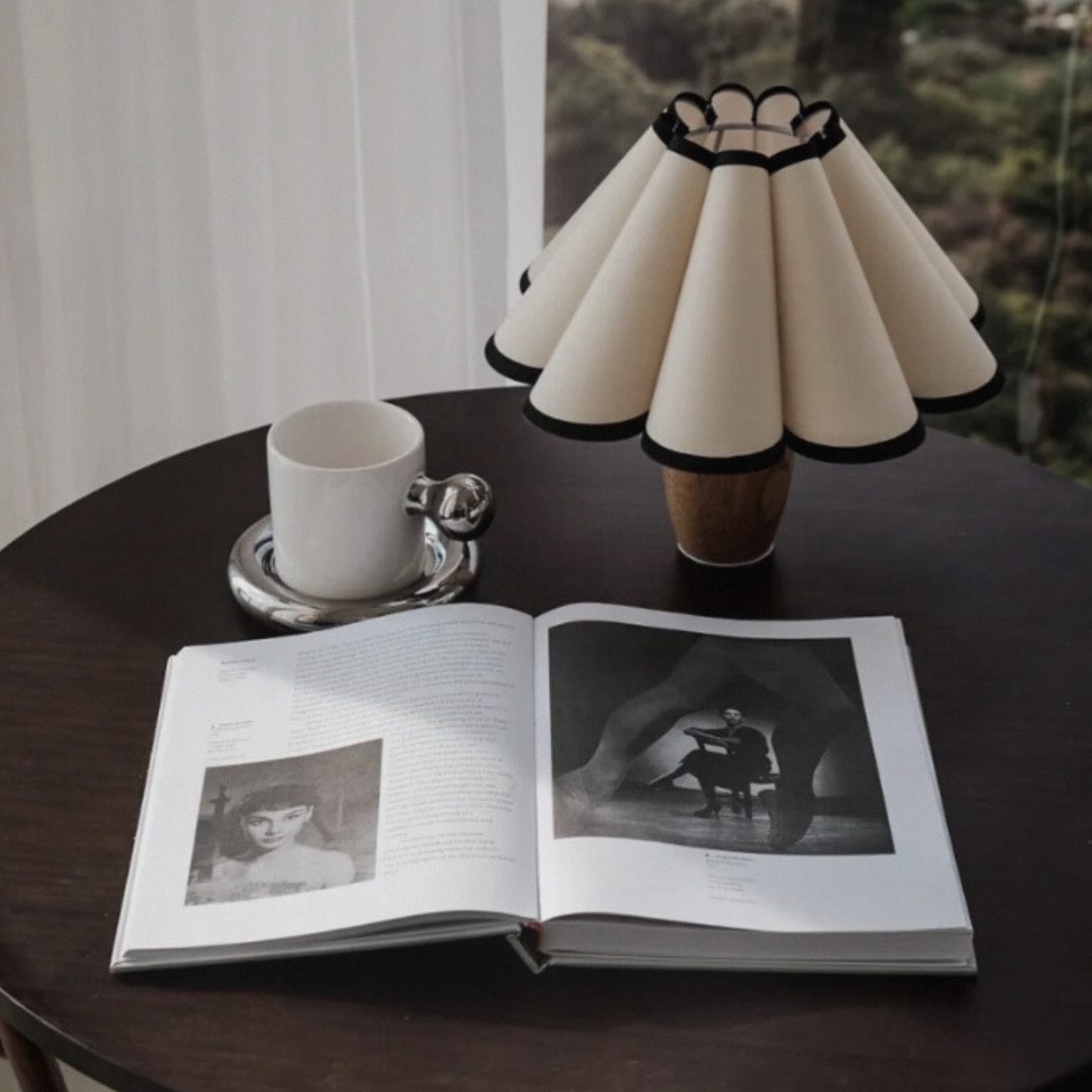 Classic table lamp with black trim and pleated shade, styled on a dark wood table with an open book, perfect for minimalist and French-inspired interiors.