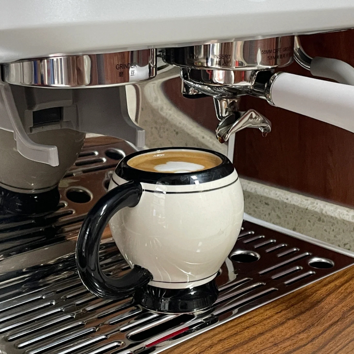 Coffee mug placed on espresso machine, showcasing sleek black and white design.