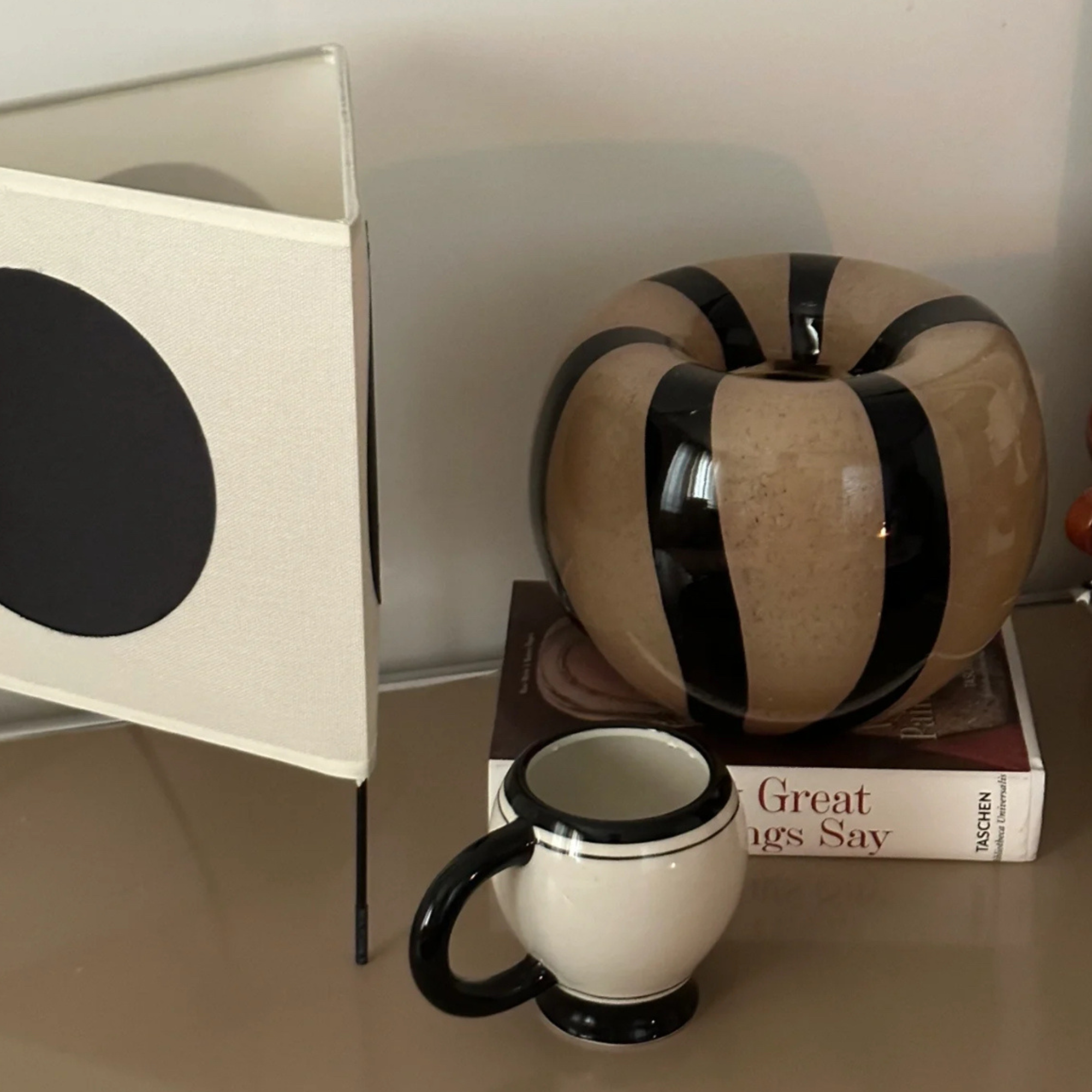 Coffee mug with black and white details, placed next to modern decor including a striped vase and a book.