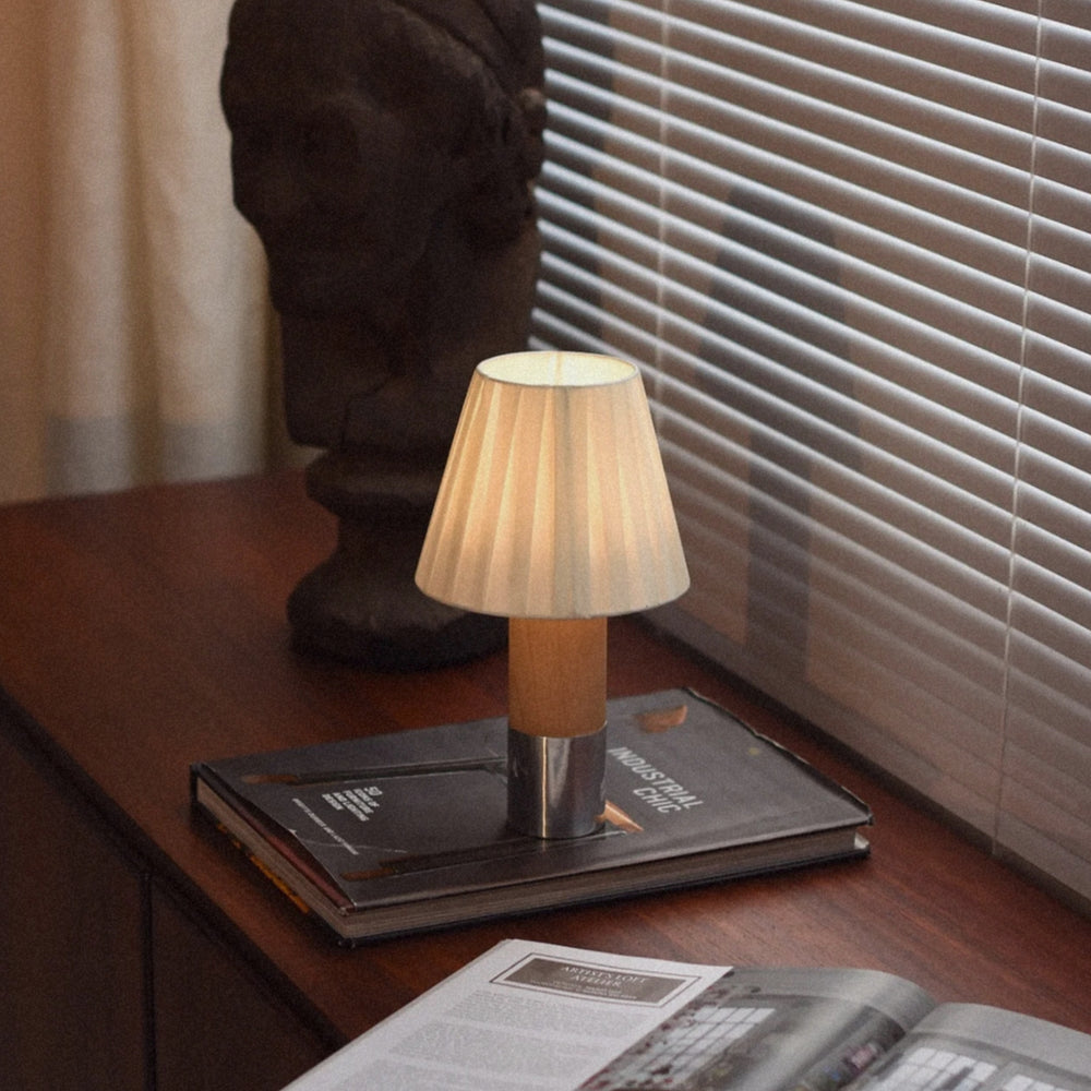 compact table lamp with pleated fabric shade set on top of books.