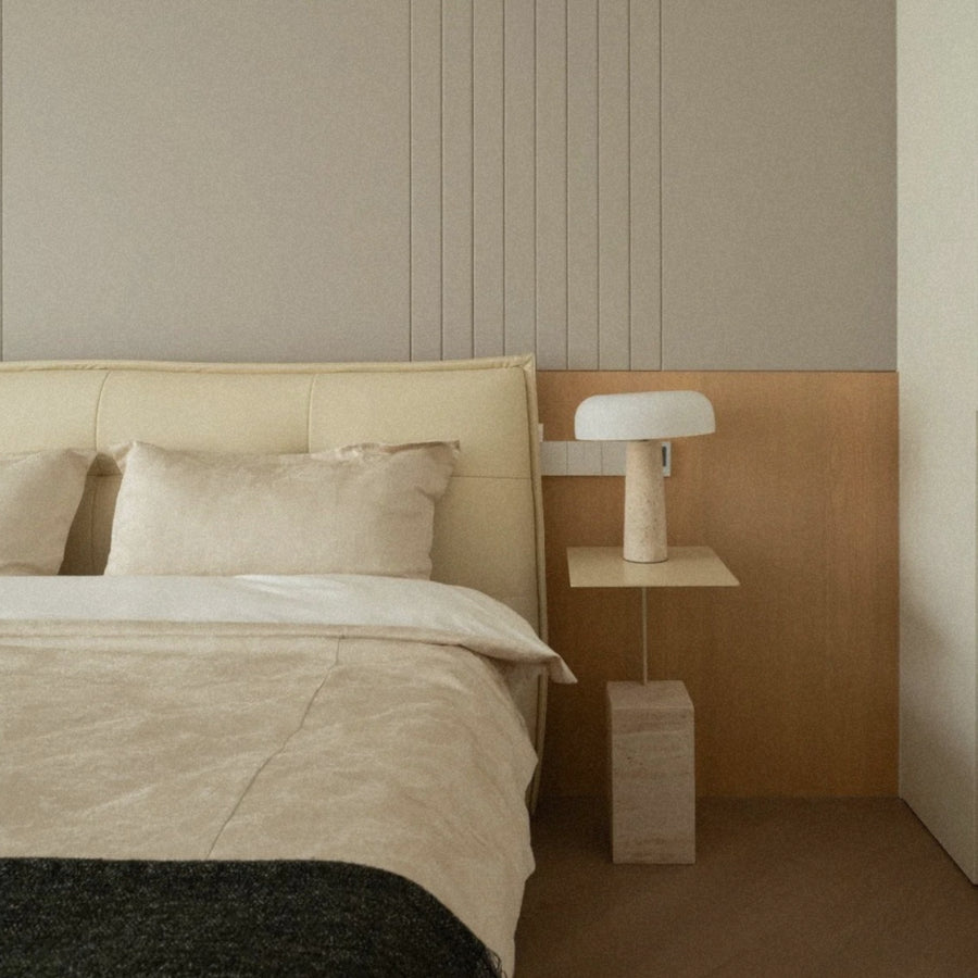 contemporary bedside table lamp made from travertine stone illuminating a calm minimalist bedroom.