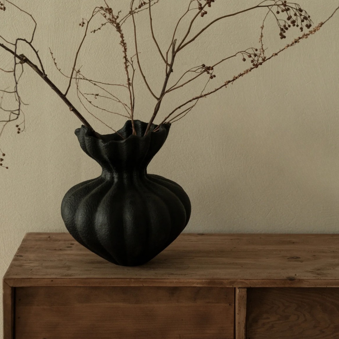 Contemporary black vase with dried branches on wooden table, adding a touch of nature to chic interiors