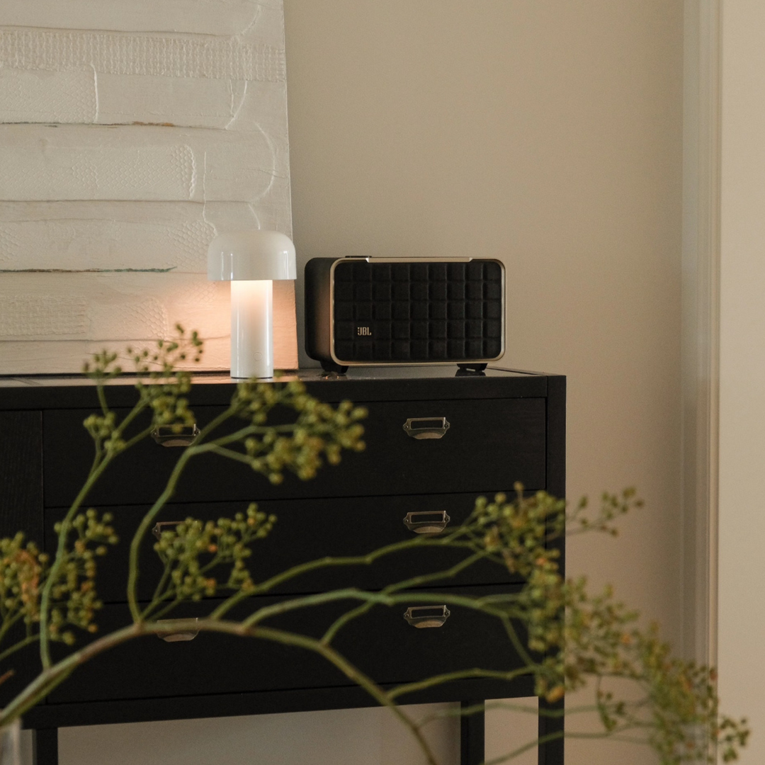 A cordless mushroom lamp sitting on a black cabinet with decor and soft greenery.