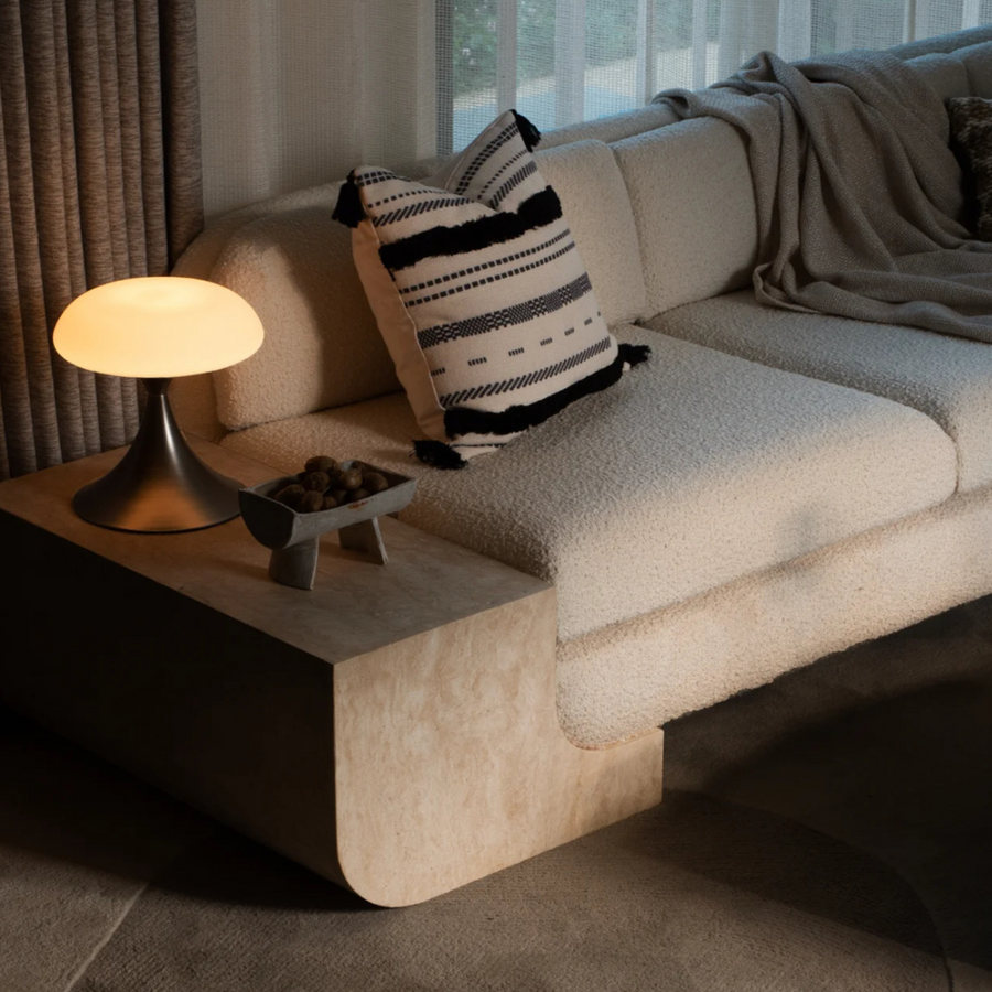 A stylish lamp with a soft glow placed on a side table in a warm, cozy living room featuring textured decor.