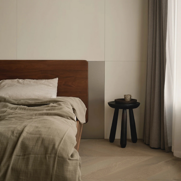 Dark wooden side table placed in a minimalist bedroom, adding warmth and texture to the space.