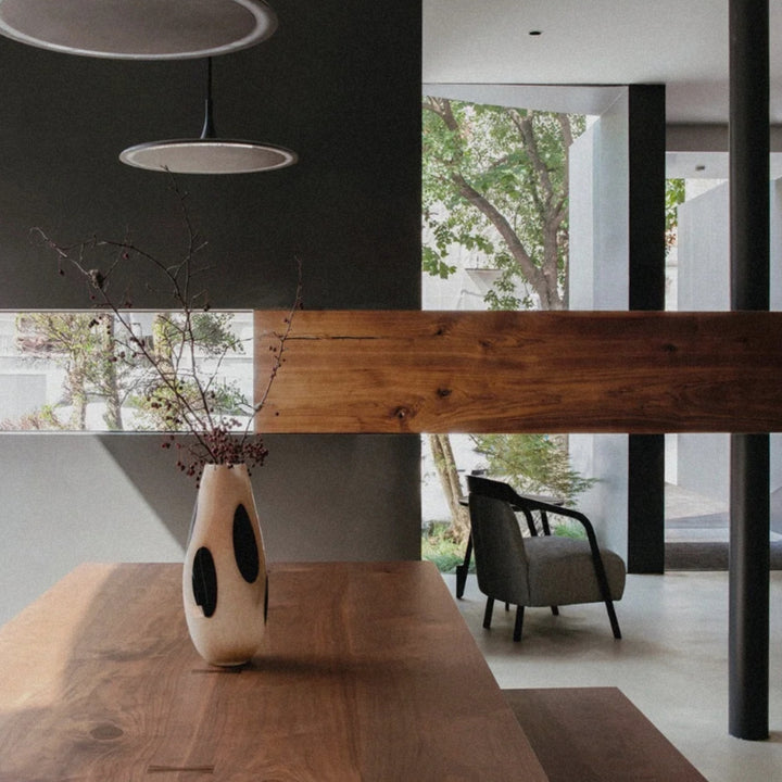 branches arranged in a glass vase create a quiet centerpiece on a long wooden table.