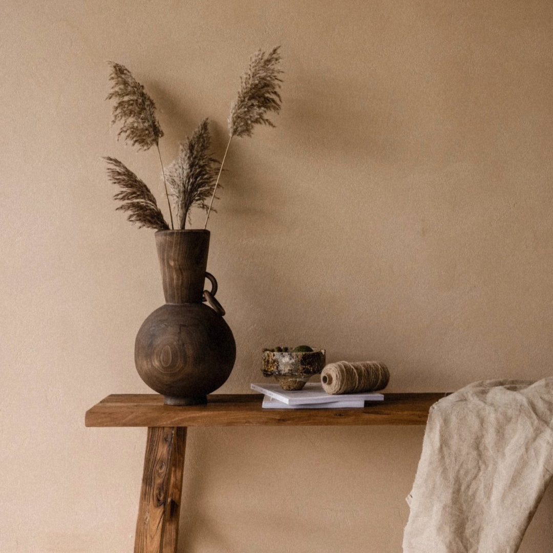 decorative wooden vase holding dried grasses placed on a simple wooden table.