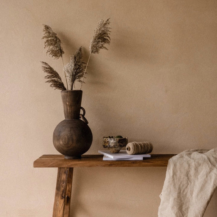 decorative wooden vase holding dried grasses placed on a simple wooden table.
