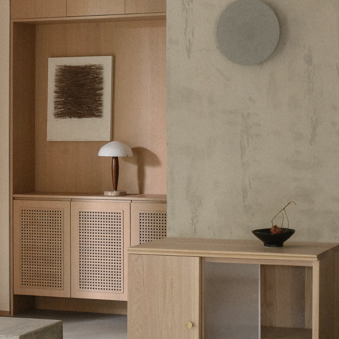 a designer table lamp combining walnut wood and marble stands on a cabinet in a minimalist interior.
