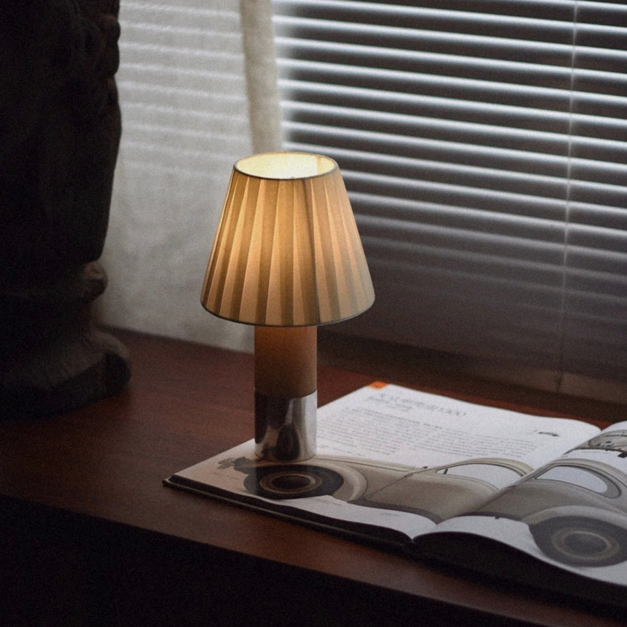 table lamp with pleated shade positioned on a desk next to an open magazine.