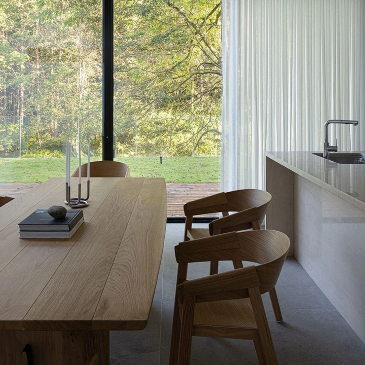 Modern stainless steel candle holder on a wooden dining table with a scenic outdoor view.