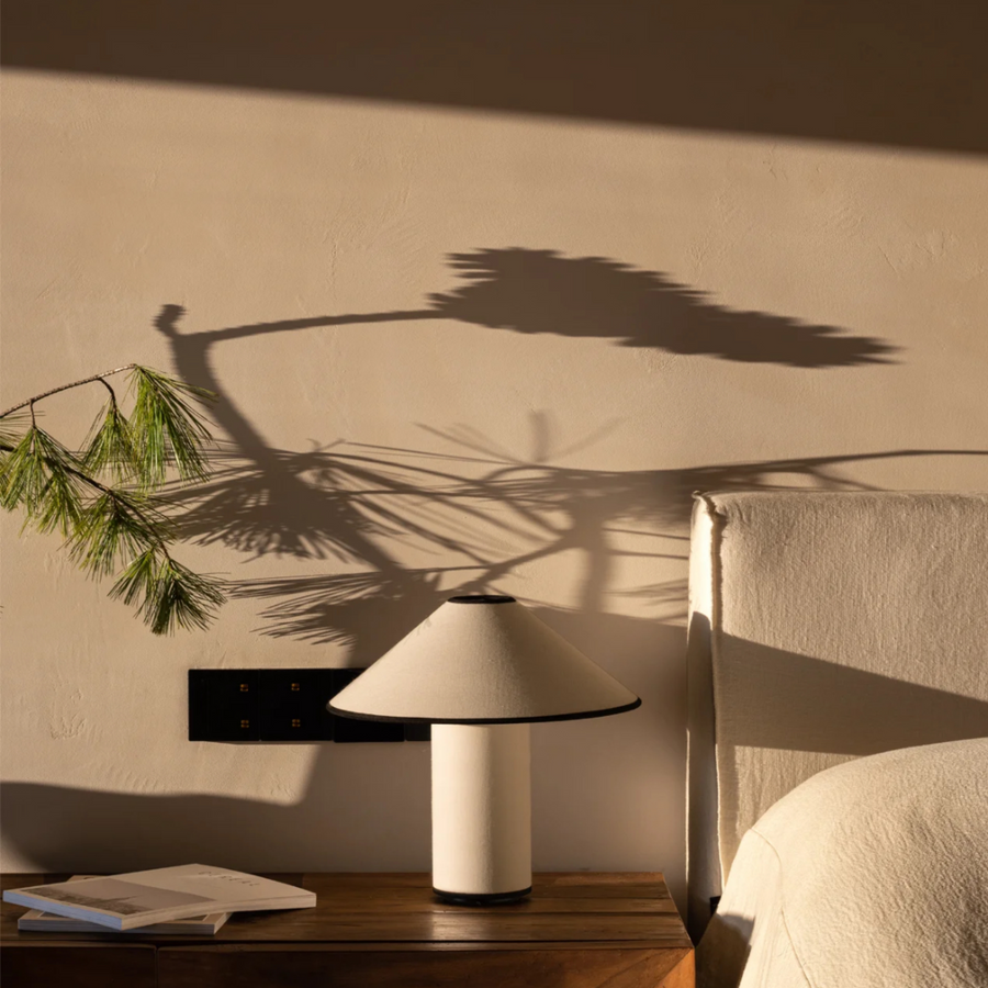 Elegant bedroom illuminated by a French-inspired table lamp, casting soft shadows on a neutral palette.