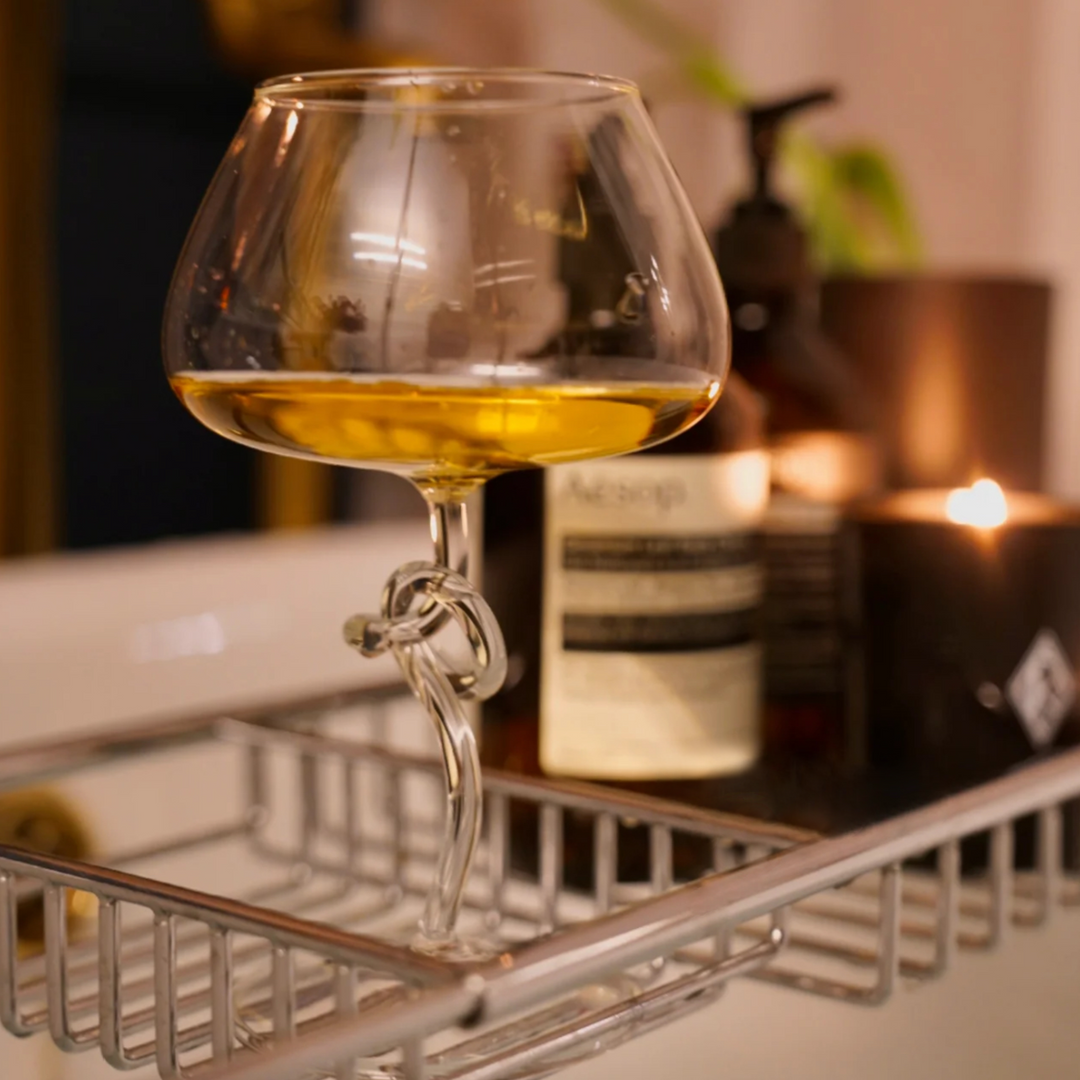 An elegant modern wine glass filled with white wine, placed on a bath tray in a luxurious, relaxing bathroom setting.