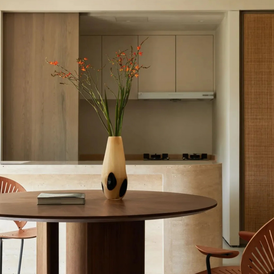 Elegant vase on a circular dining room table with natural light and minimalist design.