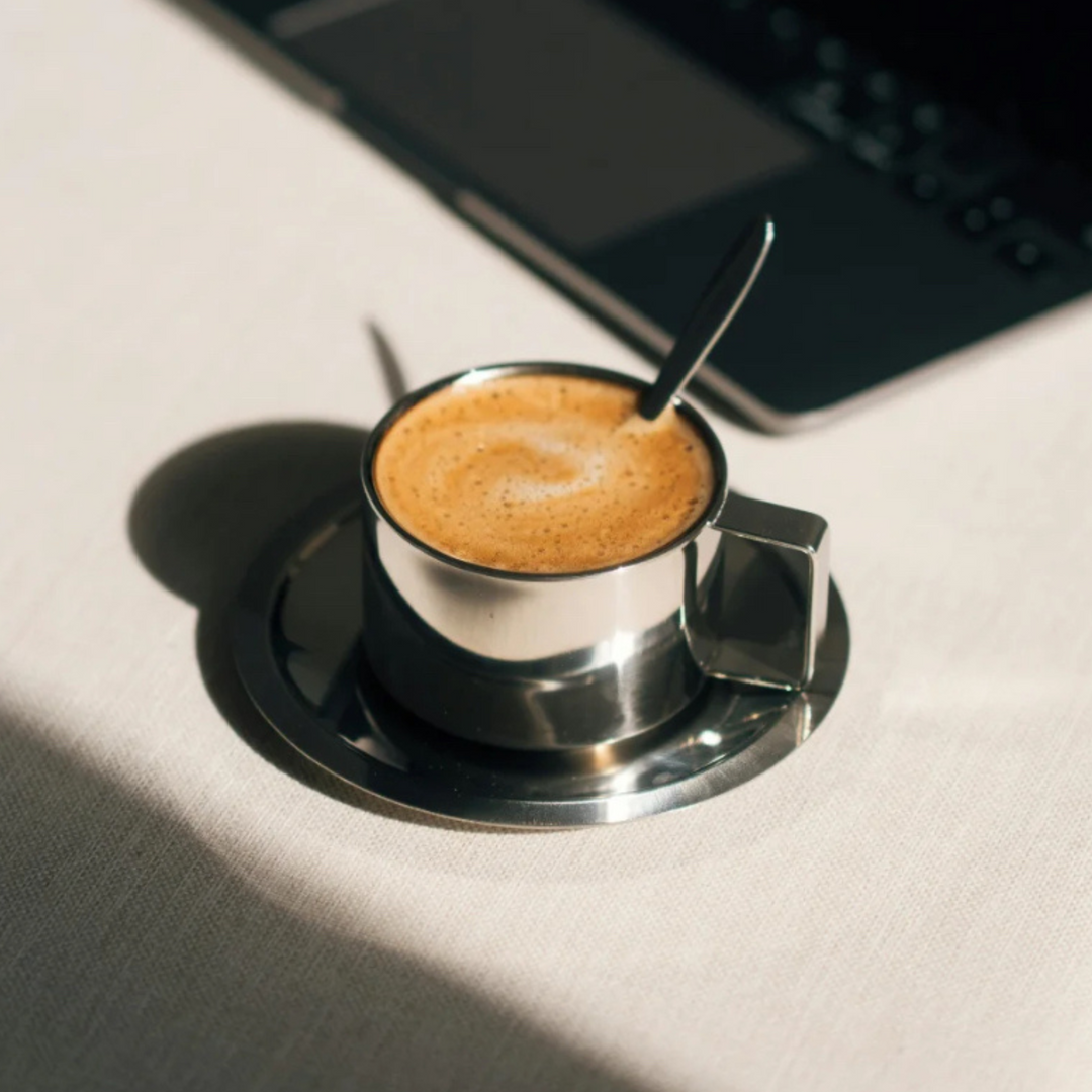 Sunlit stainless steel espresso cup on a modern desk, ideal for a stylish coffee break.