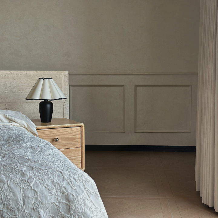 A table lamp with a black base and a cream-colored scalloped shade, enhancing the elegant and timeless French bedroom design.