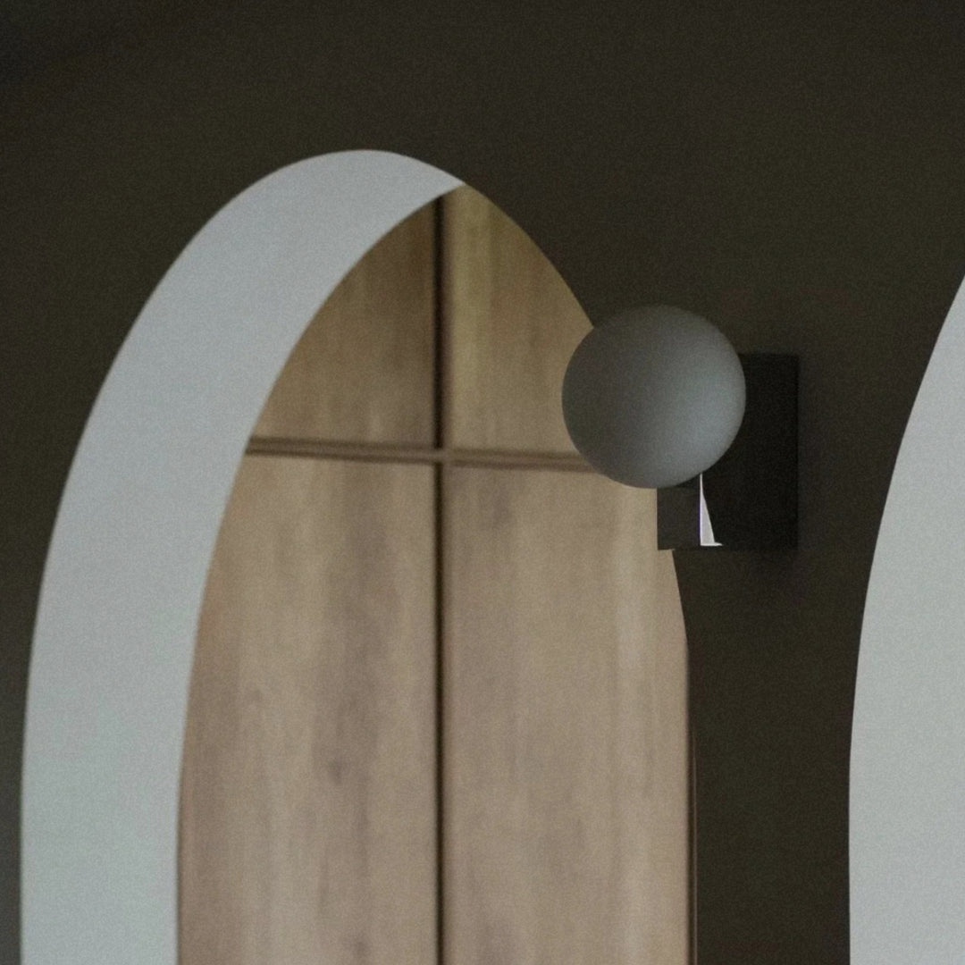 glass globe wall light mounted near an arched wall opening with a metal base.