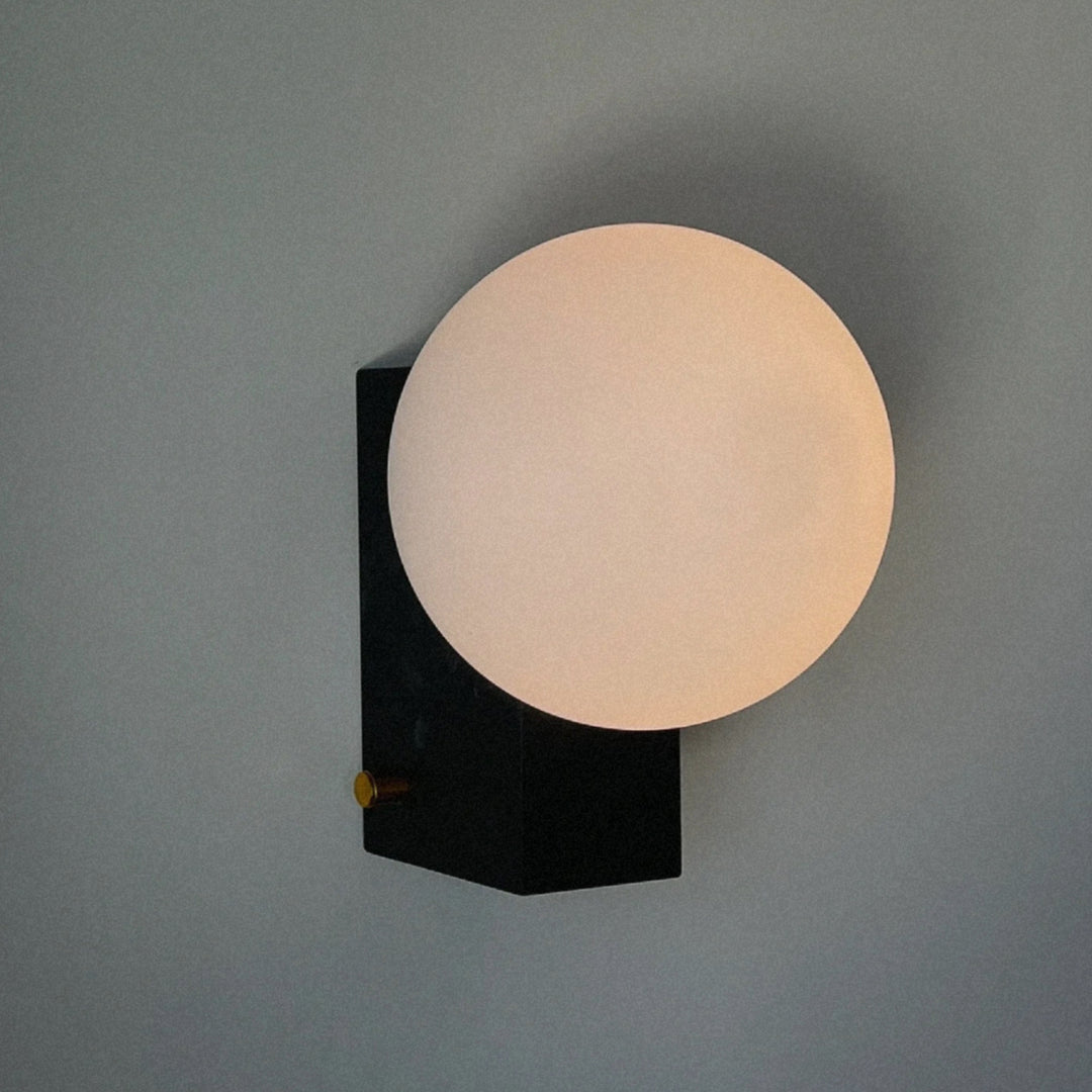glass globe wall sconce mounted on a dark metal backplate emitting soft diffused light.