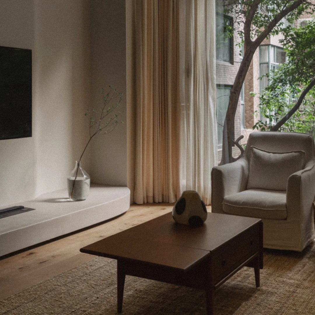 a glass vase placed on a coffee table in a calm living room with large windows and soft curtains.